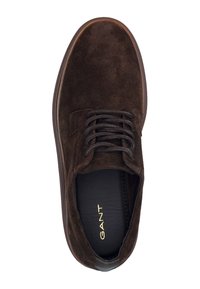 Hnědé semišové boty s kulatou špičkou, texturovaným povrchem a tmavými šňůrkami. Uvnitř se nachází zlaté logo a kontrastní tmavý okraj podrážky.