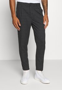 Grå rutiga byxor med tapered passform, med en knappknäppning och sidofickor, kombinerat med vita sneakers.