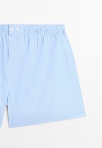 Boxer in cotone azzurro chiaro con un motivo a coste testurizzato. Presentano una cintura elastica e due bottoni bianchi sul davanti.