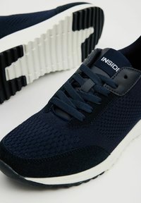 Zapatillas deportivas azul marino con un upper de malla texturizada, acentos de ante suave, suela de goma blanca y un patrón de tracción negro. Cordones en color a juego.