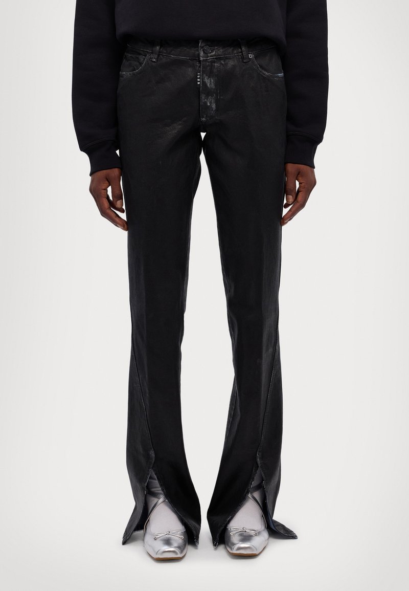 Black, high-waisted, flared pants with a shiny finish, featuring side slits. Paired with metallic silver footwear and a dark top.