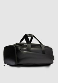 Bolsa de lona negra hecha de cuero suave con forma rectangular. Cuenta con dos asas superiores y un cierre de cremallera a lo largo de la costura superior.