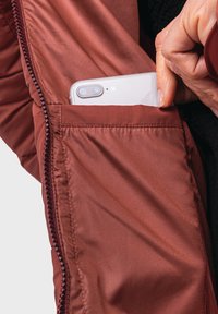Braune Jacke aus glattem, glänzendem Stoff mit einer Reißverschlusstasche für ein Smartphone. Das Innere ist gefüttert und hat eine strukturierte Naht.