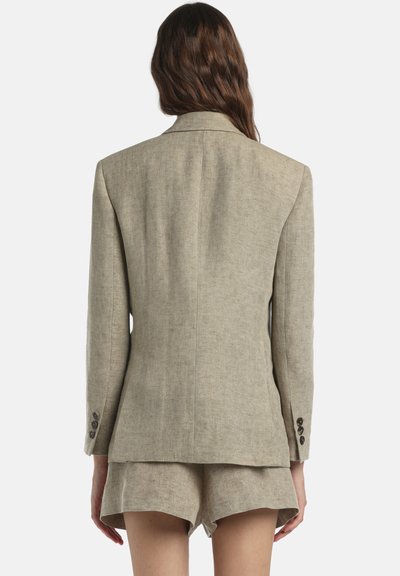 Bézs színű vászonblézer testreszabott szabással, egy hátsó sliccel és három gombos mandzsettával. Hozzá illő rövidnadrággal párosítva. Simább textúrájú.