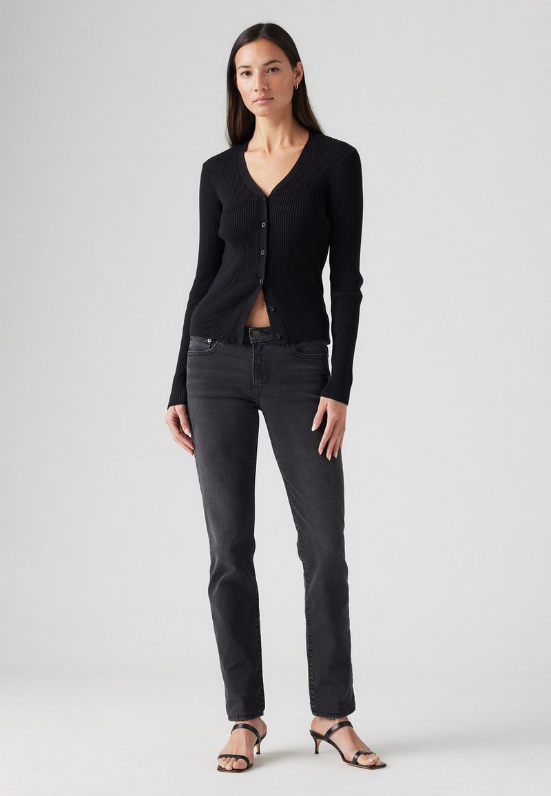 Cardigan noir côtelé avec un col en V et cinq boutons, associé à un jean droit gris foncé et des talons à brides noirs.