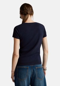 Námorně modré pletené tričko s krátkým rukávem a kulatým výstřihem, spojené se světle modrými denimovými džíny s zadními kapsami a kontrastním prošíváním.