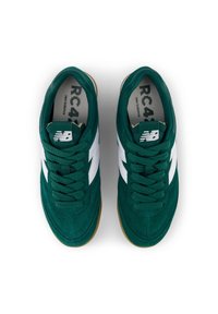 Baskets en velours vert avec accents blancs, bout rond et lacets plats. Présentent un logo en relief sur la languette et une semelle en caoutchouc.