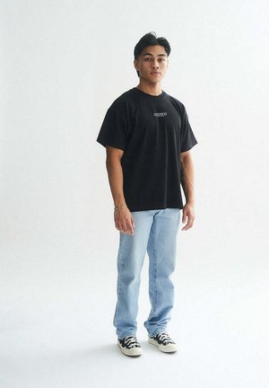 Black short-sleeve t-shirt with a small logo on the front, paired with light blue jeans and black and white patterned sneakers.
