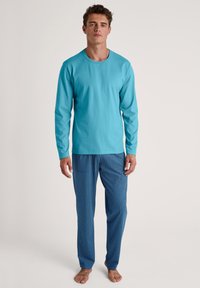 Langsleeve turkoois katoenen shirt gecombineerd met blauwe pyjamabroek met een klein wit stippenpatroon. Minimalistisch ontwerp, ontspannen pasvorm.