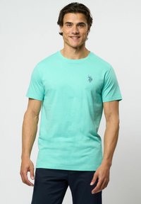 Mintgrön bomullströja med korta ärmar, rundad halsringning och en liten mörk logotyp på vänster bröst. Slät textur, avslappnad passform.