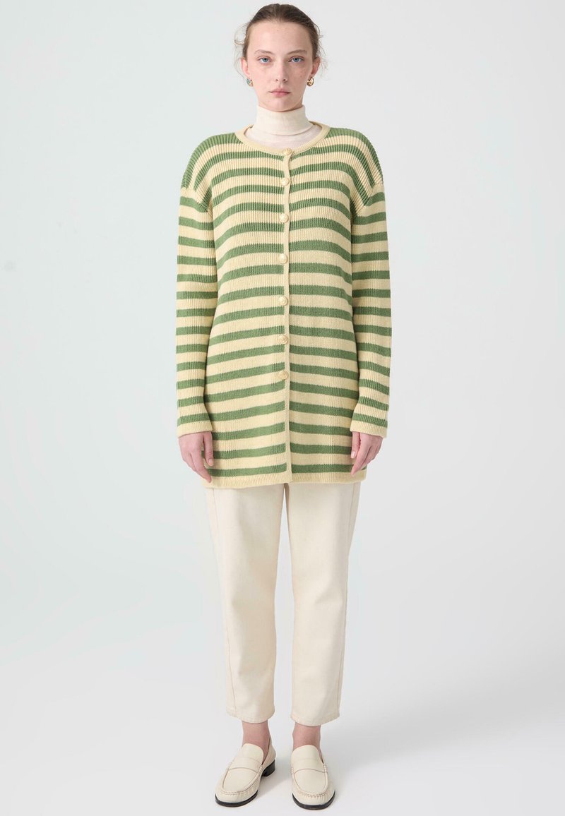 Grön och krämrandig cardigan med ribbad textur, långa ärmar och knäppning, i kombination med krämfärgade byxor och loafers.