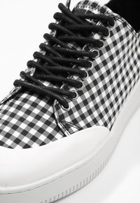Baskets à carreaux noir et blanc avec lacets noirs et semelle en caoutchouc blanche, gros plan montrant le motif et les œillets.