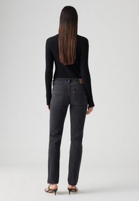 Fekete skinny farmernadrág magas derékkal, hátul bőr márkajelzéssel, sima, texturált anyagból. Karcsú fazon, egyenes szárakkal.