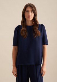 Blusa blu navy con maniche a sbuffo corte e scollatura rotonda. Tessuto morbido con vestibilità comoda, abbinata a pantaloni coordinati.