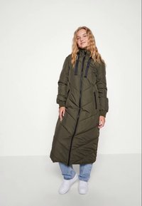 Casaco puffer longo, verde-azeitona, com um alto colarinho, fecho de correr preto e bolsos laterais; apresenta um padrão de quilt em chevron e punhos de mangas em malha.