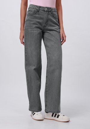 Onderlichaam met high-waist grijze rechtvallende jeans, gecombineerd met witte sneakers met zwarte strepen.