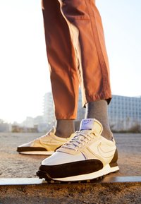 Sneakers in beige en zwart met mesh en suede materialen. Voorzien van een witte zool, een gestructureerde bovenkant en een paarse accent op de tong.