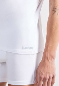 Valkoinen Sloggi-t-paita ja shortsit, pehmeää puuvillamateriaalia, istuva muotoilu, subtile logo painettuna paidan helmaan.