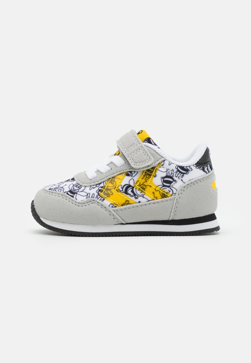 Grijze suede sneaker met bovenwerk van wit en geel canvas met een cartoonpatroon, klittenbandsluiting en een zwarte rubberen zool met witte rand.