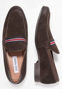 Mocassins en daim marron avec un bout légèrement arrondi. Présente un accent textile rayé sur le dessus. Semelle plate en caoutchouc marron. Intérieur doublé.