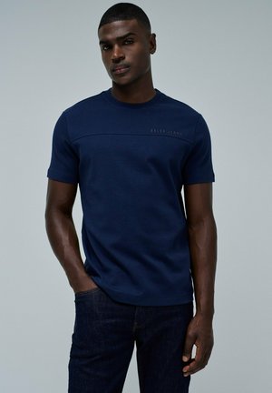 Camiseta de manga corta azul marino hecha de un tejido suave, con una costura horizontal y un discreto logotipo bordado de "Salsa Jeans" en la parte delantera.