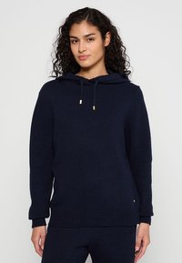 Marineblaue Kapuzenpullover mit gerippter Textur, Kordelzugverschluss und goldenen Akzenten. Verfügt über eine lockere Passform und lange Ärmel.