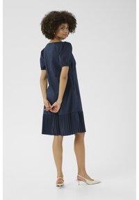 Tmavomodré šaty s krátkymi nadýchanými rukávmi, skladaným spodným okrajom a voľným strihom. V kombinácii s béžovými lodičkami, zobrazené zozadu.