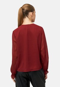 Bordeauxrode blouse met lange, doorschijnende mouwen en een losse pasvorm. Voorzien van gerimpelde manchetten en een ronde halslijn. Gladde textuur, lichtgewicht stof.