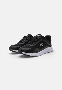 Chaussures de sport noires avec une tige en maille, des accents texturés et une semelle blanche avec des crampons noirs. Comprend des lacets et un logo sur le côté.