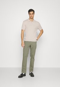 Helles rosa strukturiertes Polohemd mit kurzen Ärmeln, kombiniert mit olivgrünen Hosen und schwarzen Slippern. Einfaches, sauberes Design, ohne sichtbare Muster.