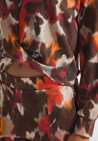 Set di abbigliamento da lounge multicolore, realizzato in un tessuto morbido e texturizzato con un motivo astratto nei toni di rosso, arancione e marrone. Include un dettaglio a torsione nella parte superiore.