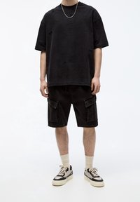T-shirt noir oversize avec des trous usés, associée à un short cargo noir avec des poches latérales. Complété par des baskets noires et blanches.