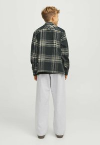 Svart och grönrutig flanellskjorta med knapp-down krage, tillsammans med löst sittande ljusgrå byxor. Visar bakifrån.