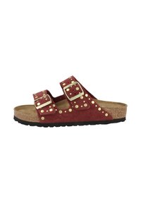 Rode suède slide-sandaal met twee verstelbare banden, gouden studs en een getextureerde kurken voetbed. Zwarte rubberen buitenzool.