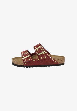 Infradito in suede rosso con due cinturini regolabili, dettagli in oro e una soletta in sughero texturizzato. Suola in gomma nera.