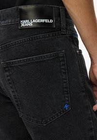 Jeans de mezclilla negra con una etiqueta de cuero y costuras azules. Cuenta con bolsillos estándar y una silueta de pierna recta.