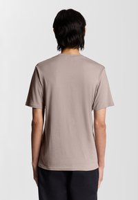 T-shirt in cotone beige con una vestibilità rilassata, maniche corte e un semplice collo a giro. Il tessuto appare morbido con una consistenza liscia.