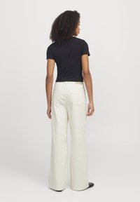 T-shirt preto ajustado combinado com calças largas em creme, exibindo uma textura suave e dois bolsos nas costas. Usado com calçado preto.