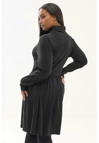 Czarna sukienka z długim rękawem, z wysokim kołnierzem, dopasowaną górą i rozkloszowanym dołem. Gładki materiał z teksturowanym wykończeniem w talii.