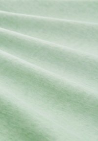 Tissu en coton vert clair avec une texture lisse, présentant de douces ondulations et des variations subtiles de couleur sur la surface.