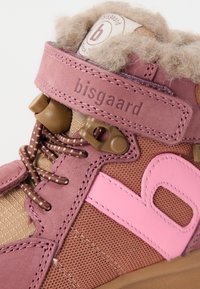 Närbild av en rosa och brun barnsnörskon med fleecefoder, elastiska snören och ett kardborreband märkt "bisgaard."
