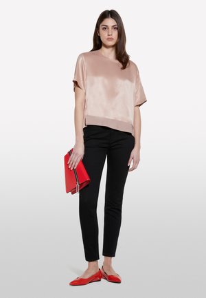 Top corto di satin color rosa pallido con maniche corte abbinato a pantaloni neri attillati e scarpe basse rosse. In mano una pochette rossa con dettaglio zip.