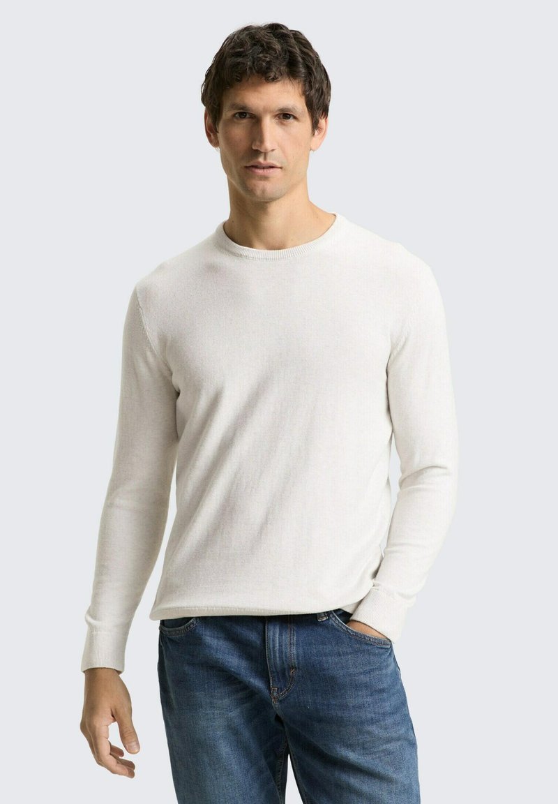 Hellbeiger langärmeliger Pullover mit rundem Ausschnitt, gerippten Bündchen und weicher Textur, kombiniert mit blauen Denim-Jeans.