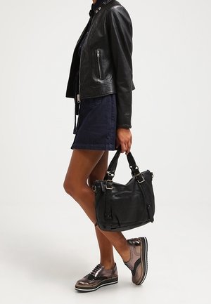 Borsa in pelle nera con superficie texture e due manici robusti, abbinata a un outfit scuro e scarpe brogue lucide.