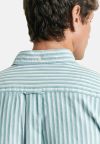 Camisa a rayas azul claro y blanca con una textura suave, con cuello abotonado, yugo trasero y un solo pliegue en la parte trasera.
