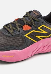 Scarpa sportiva nera con accenti gialli, sovrapposizione testurizzata, dettagli arancioni e suola Fresh Foam rosa. Parte superiore in mesh leggera per traspirabilità.