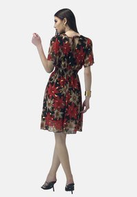 Vestido floral con mangas cortas, base negra, flores rojas y doradas, cintura ceñida, y detalle de abertura en la parte trasera. Llevado con sandalias de tacón negras.