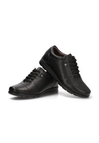 Zapatos de cuero negros con punta redondeada, superficie texturada, diseño con cordones y un pequeño acento metálico en el costado. Suela de goma flexible.