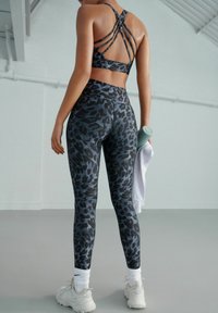 Zwarte en grijze luipaardprint sportbh met kruislings verstelbare bandjes, gecombineerd met bijpassende leggings. Bevat een gladde, rekbare stof en een hoge tailleband.