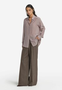 Ljuslila randig skjorta med knappar och avslappnad passform, i kombination med vida bruna byxor med texturerad tyg och sidofickor.